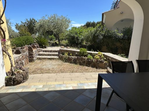 Gartenansicht mit Weg, Pflanzen und Terrasse unter blauem Himmel.