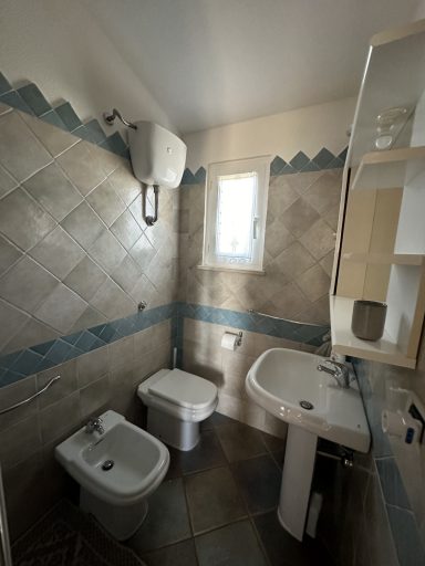 Kleines Badezimmer mit weißer Toilette, Bidet und Waschbecken, gefliestem Boden.