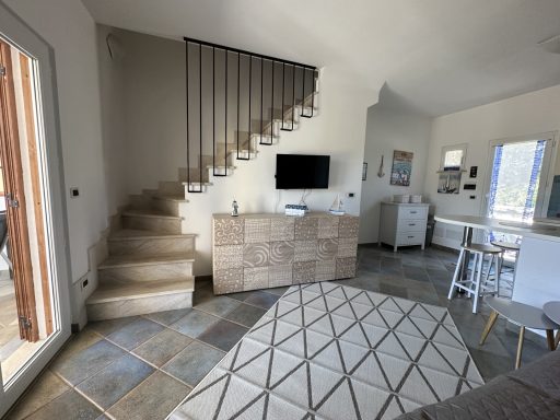 Heller Wohnraum mit Treppe, Fernseher und Essbereich, moderne Einrichtung.