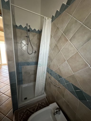 Dusche mit weißen Vorhängen und gefliestem Boden in einem hellen Raum.